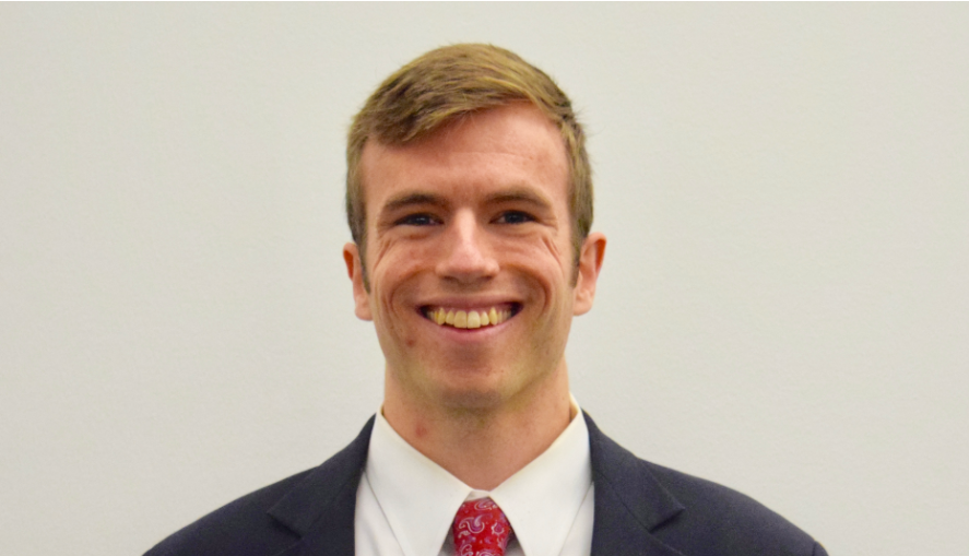 Ben Cook smiling in a blue blazer and red tie.